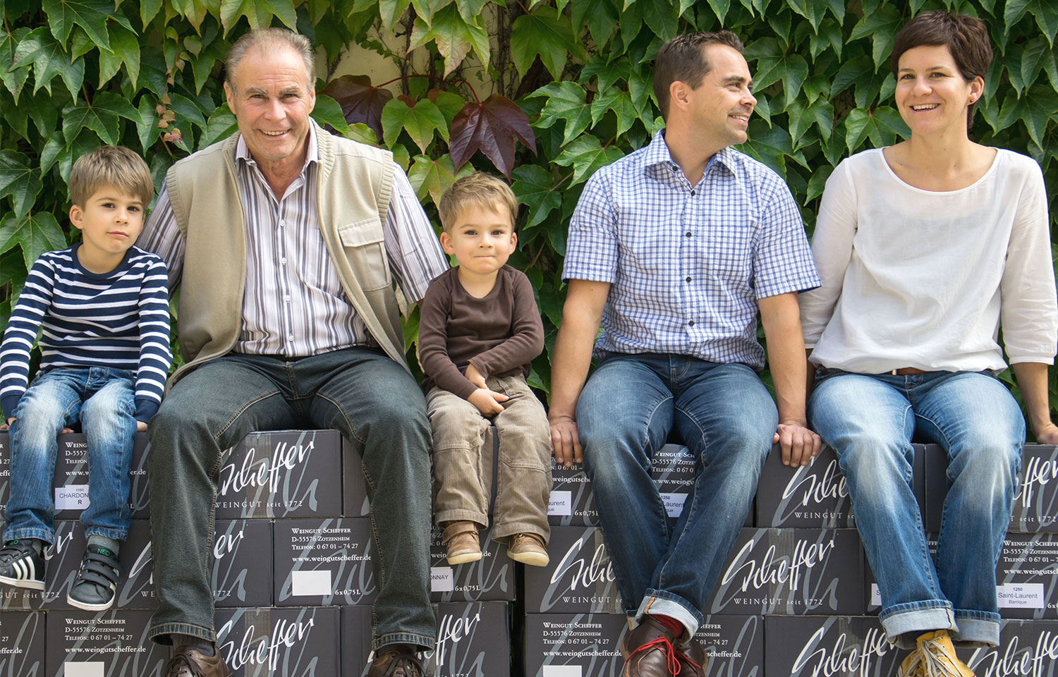 Winzer-Familie Scheffer (Mann, Frau, 2 Kinder und Großvater) sitzen auf Weinkartons. 